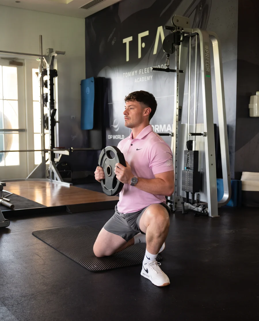 Jamie in a half kneeling lunge with a plate in front of the TFA wall